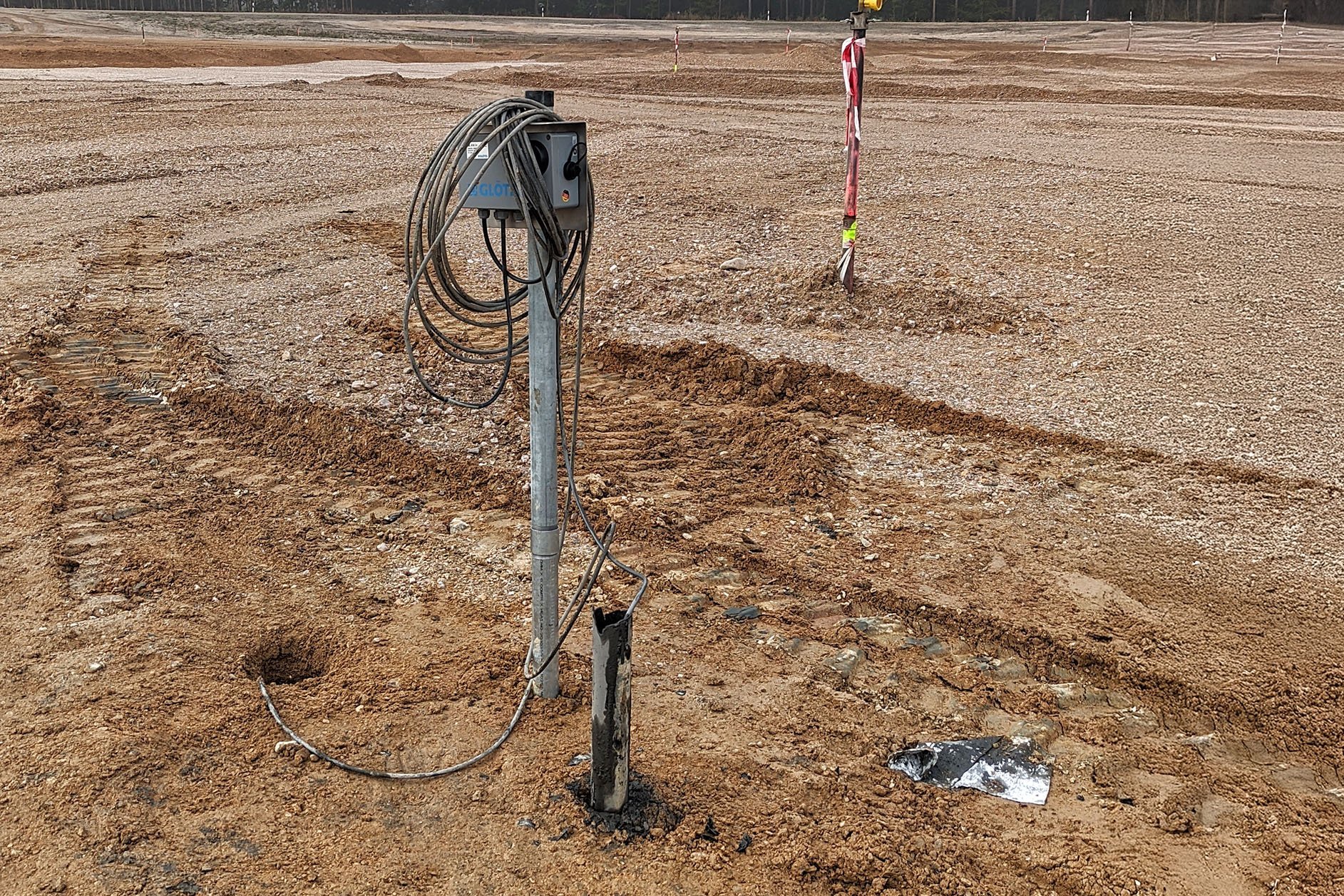 An einer Stange ist ein Kasten angebracht. In Schlaufen sind daran zwei aus dem Boden kommende Kabel aufgehängt.