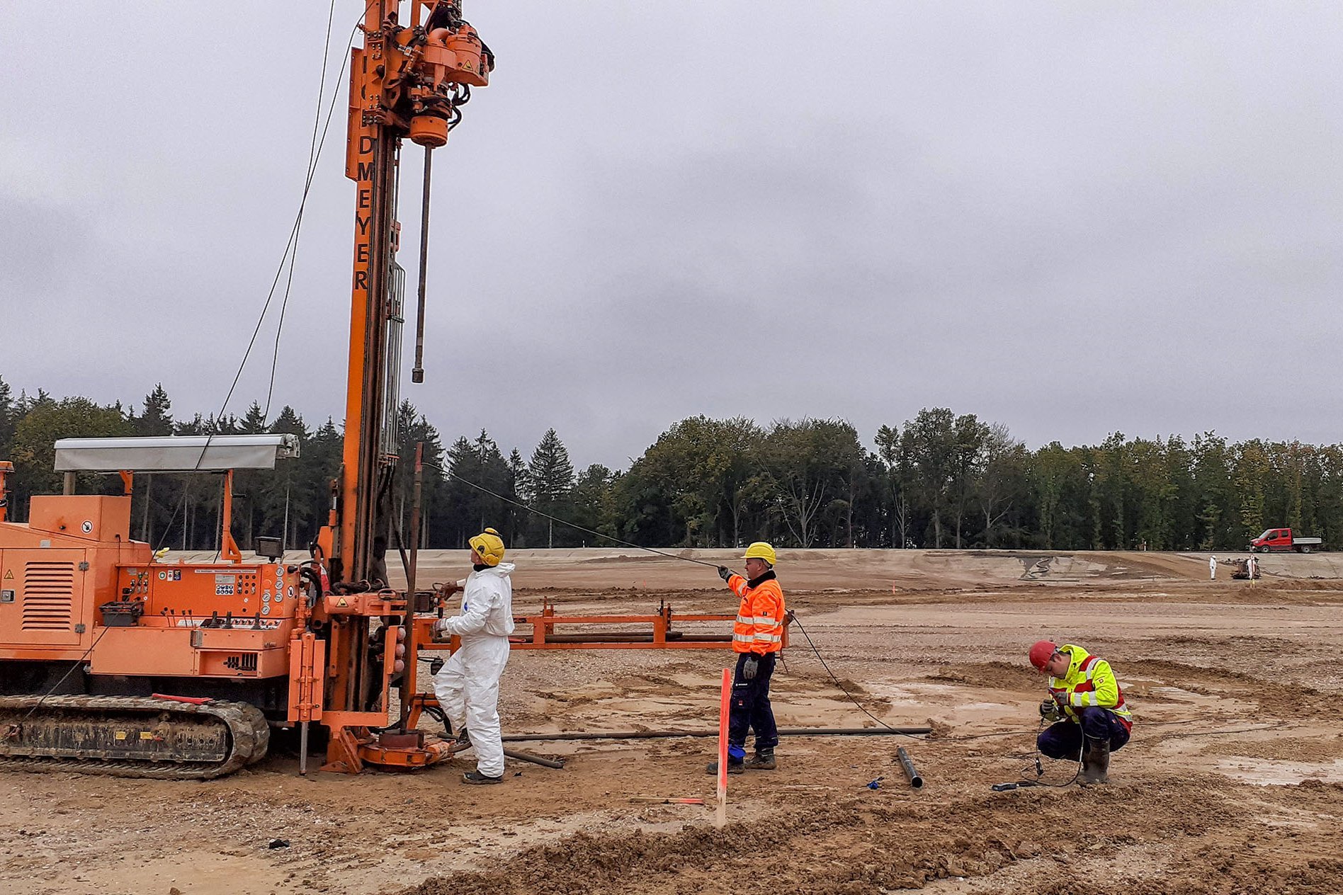 Arbeiter an einem Bohrgerät auf einem Kettenfahrgestell auf einer Ebene