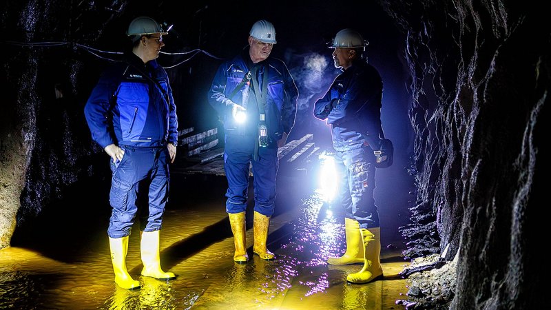 Nur von Strinlampen erhellt stehen drei Männer im Stollen