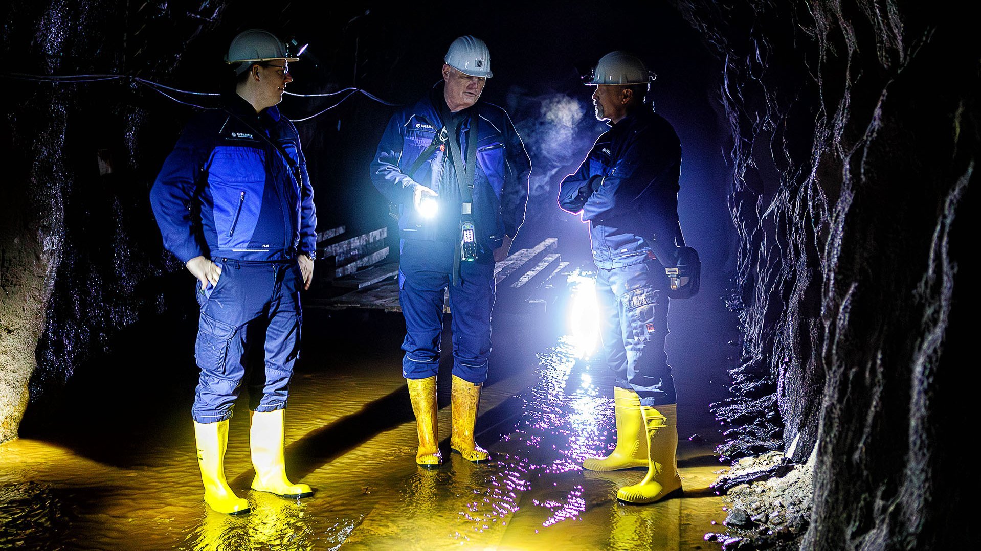 Nur von Strinlampen erhellt stehen drei Männer im Stollen