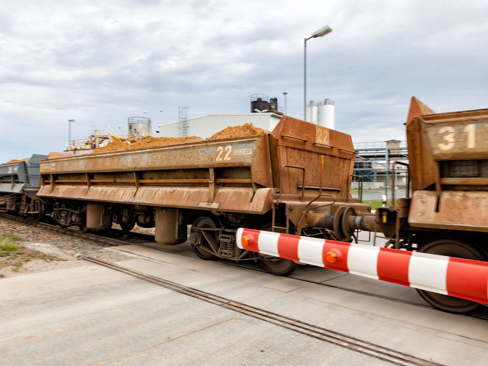 Gefüllte Wagons an einem Bahnübergang mit geschlossener Halbschranke