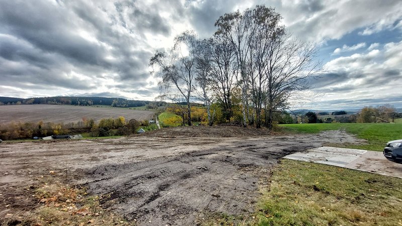 Eine Stelle in einem Feld mit glatter Erdoberfläche ohne Bewuchs. Am Rand eine kleine Halde mit Bäumen.