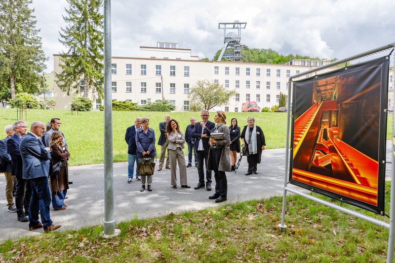 Eine Menschengruppe steht neben einem großen Foto, dahinter ist der Schcht 371 zu sehen