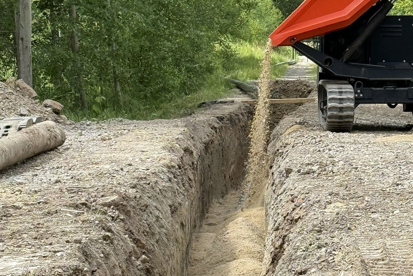 Kleiner Muldenkipper lässt Sand in einen Graben ab