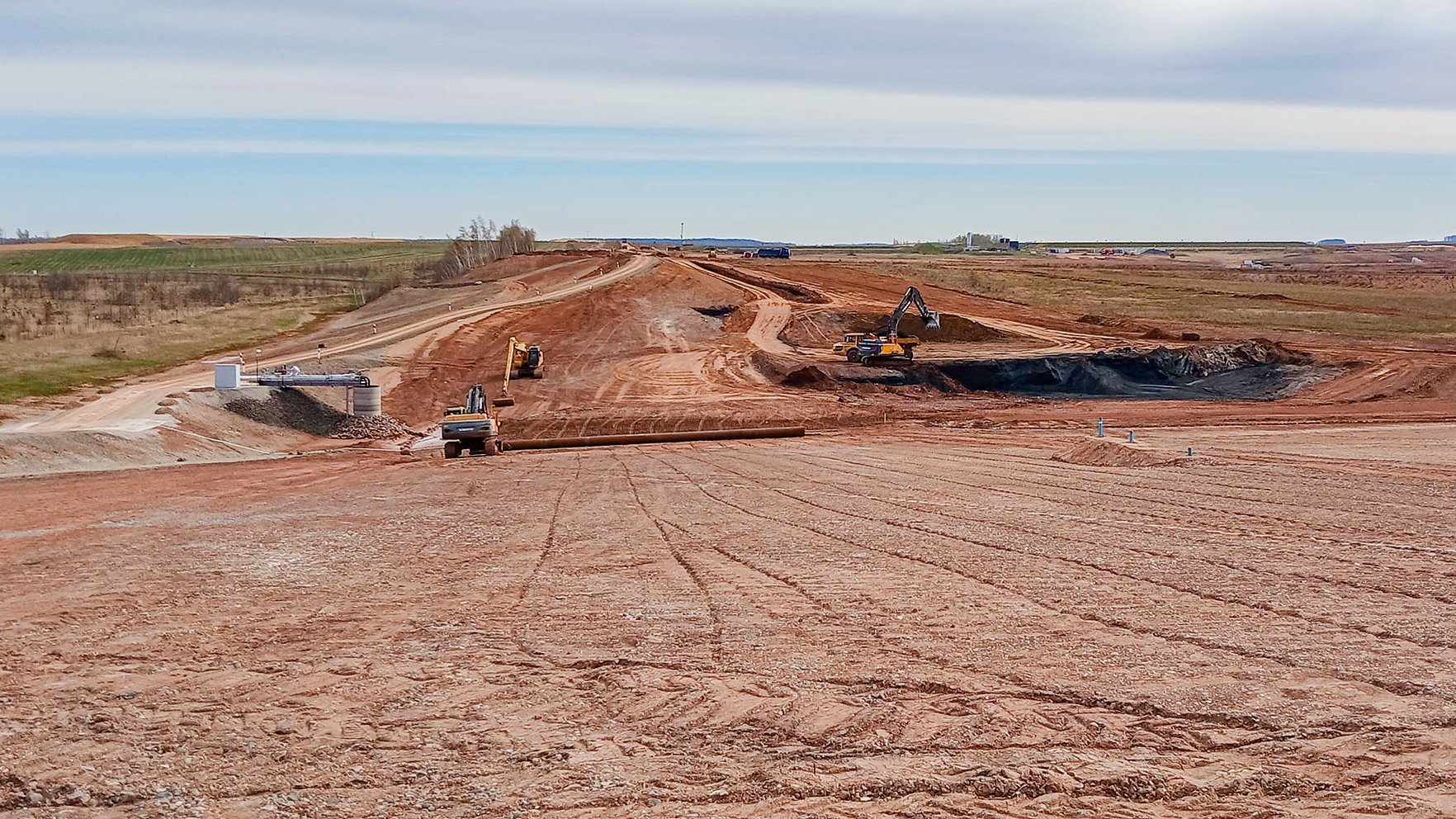 Eine Kerbe verläuft quer über das Foto, links ein Hochwasserdamm, rechts werden Tailings ausgehoben