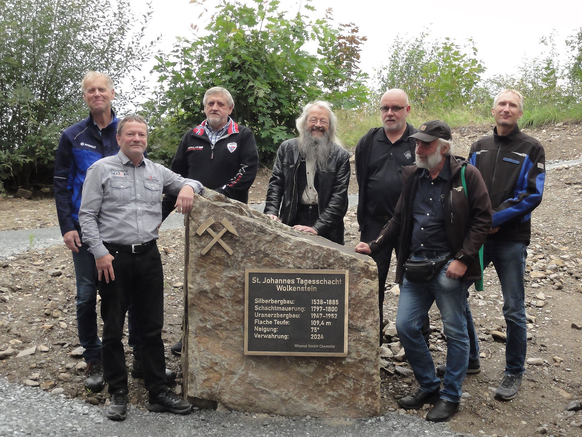 sieben Männer stehen an einem großen Stein mit den Daten zum Schacht