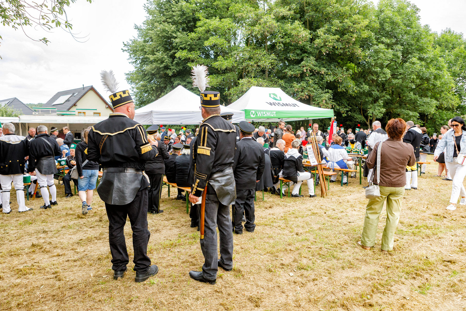 Menschen auf einer Wiese, viele in Bergmannstracht stehen oder sitzen an Pavillions an einem Imbiss