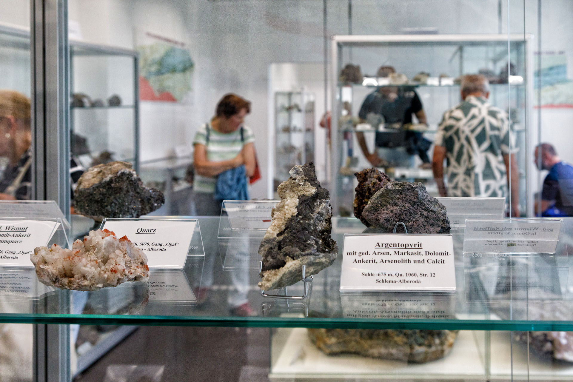 Blick über Kristalle und Minerale in einer Glasvitrine in den Ausstellungsraum mit Besuchern